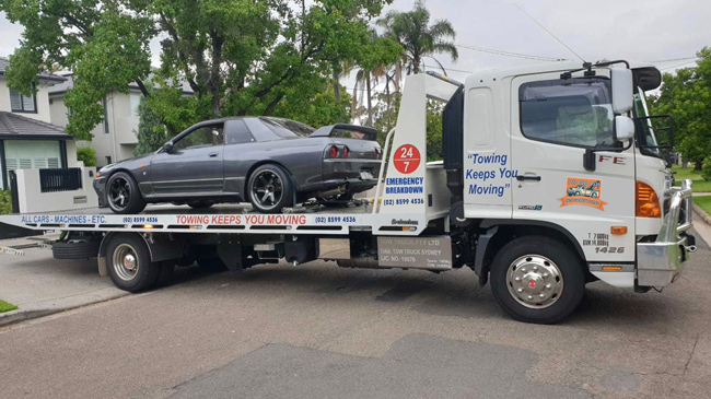 An older car being towed in a quiet Sydney suburb