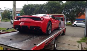 A Ferrari getting towed from a quiet Sydney suburban street on an overcast day.