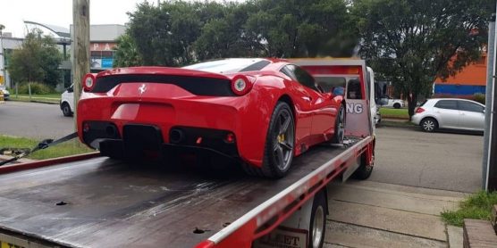A Ferrari getting towed from a quiet Sydney suburban street on an overcast day.