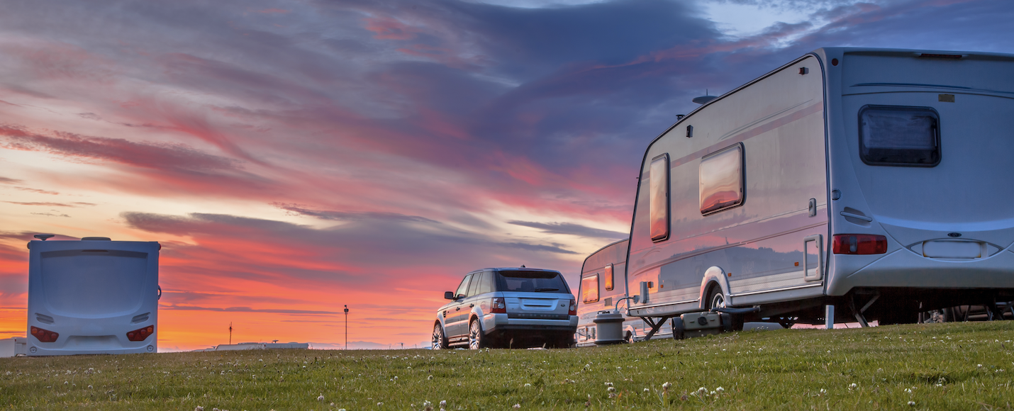 A car towing a caravan on the grass with a sunset.