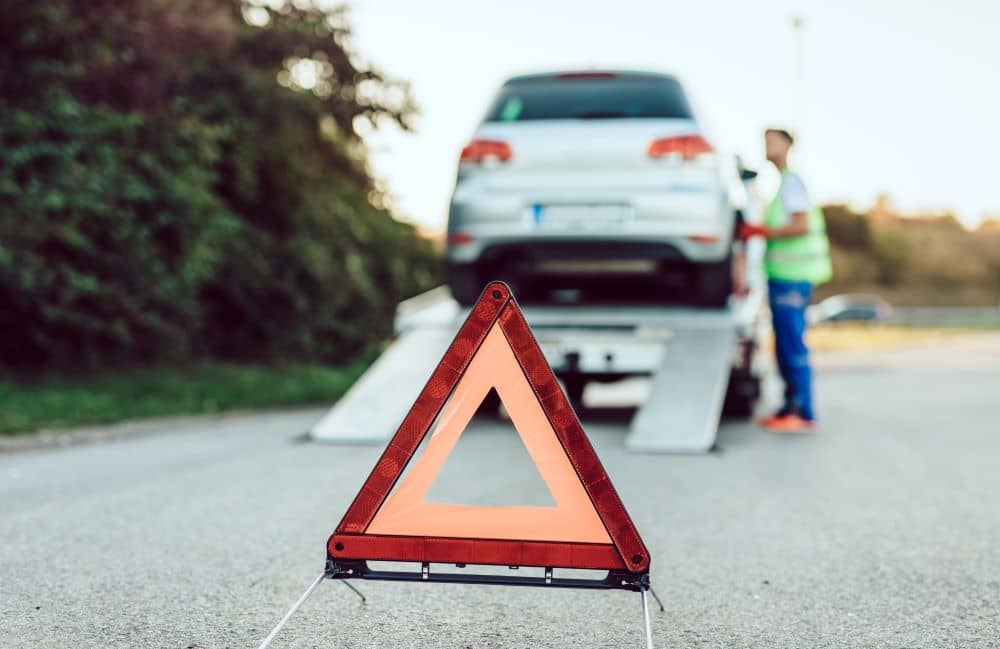 Road warning device with towed car on the side of the road in the background.