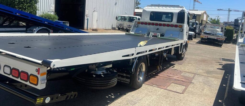 A tilt tray tow truck in the Sydney yard with the other trucks.