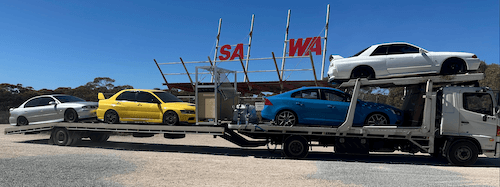 A tilt-tray truck carrying four cars across the South Australia–Western Australia border, highlighting Fast Sydney Towing’s interstate car transport services.